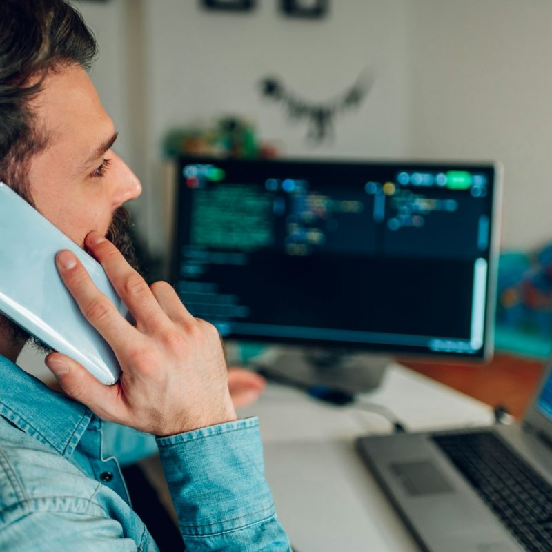 Side view of a data scientist talking on the phone. In a blurry background is a software interface.